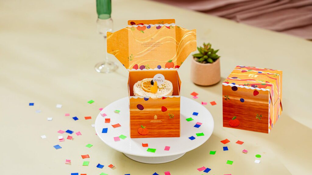 desain kotak kue berwarna orange dengan kue mini di dalamnya